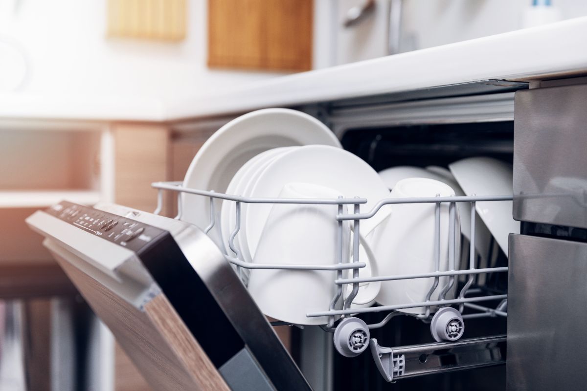 Open dishwasher with clean white plates and dishes in kitchen