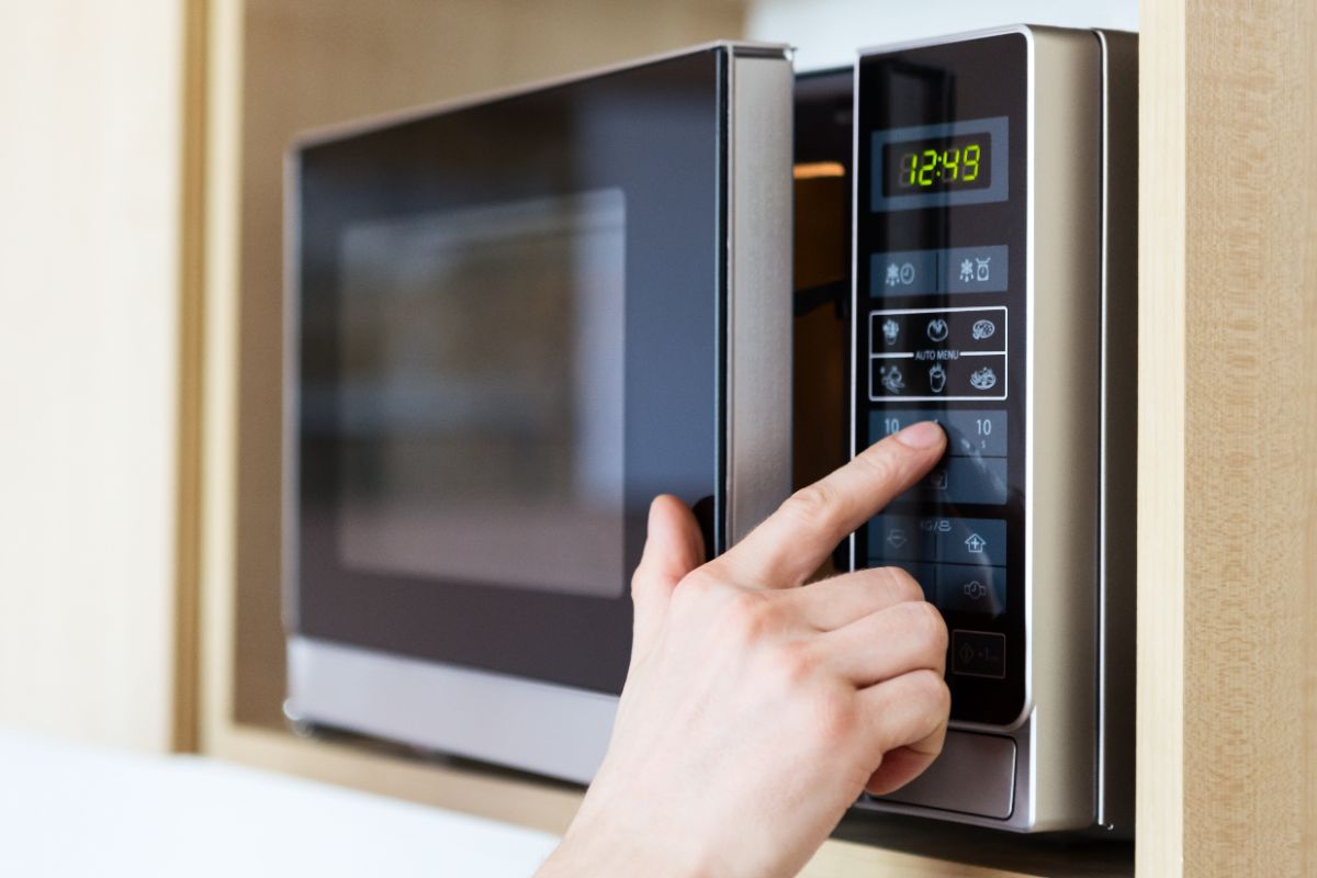 Person's hand pressing button on microwave oven control panel displaying 12:49