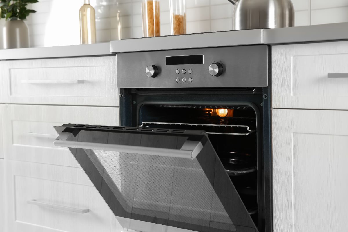 Built-in stainless steel oven with door open in modern white kitchen cabinetry