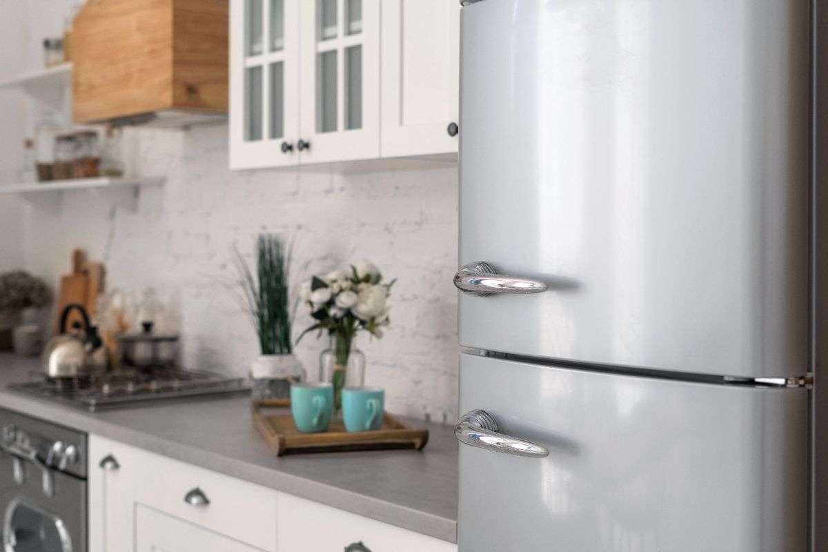 Modern white kitchen with refrigerator, marble backsplash, and fresh flowers in turquoise vases
